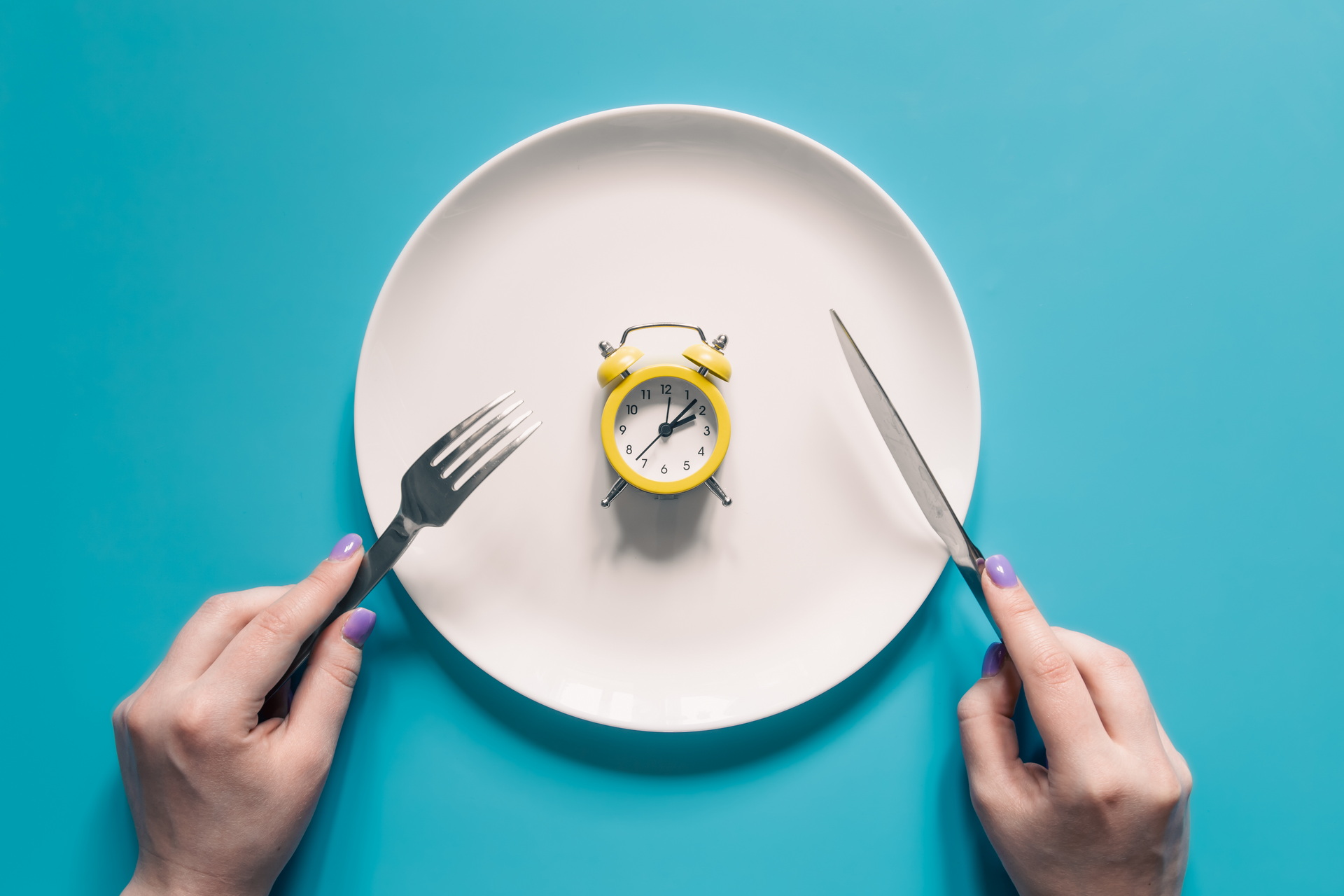 hands-holding-knife-fork-alarm-clock-plate-blue-background